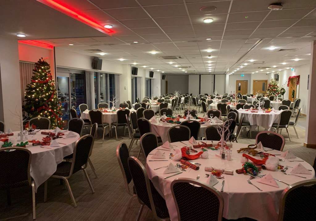 Holiday banquet hall with decorated round tables and a lit Christmas tree near large windows