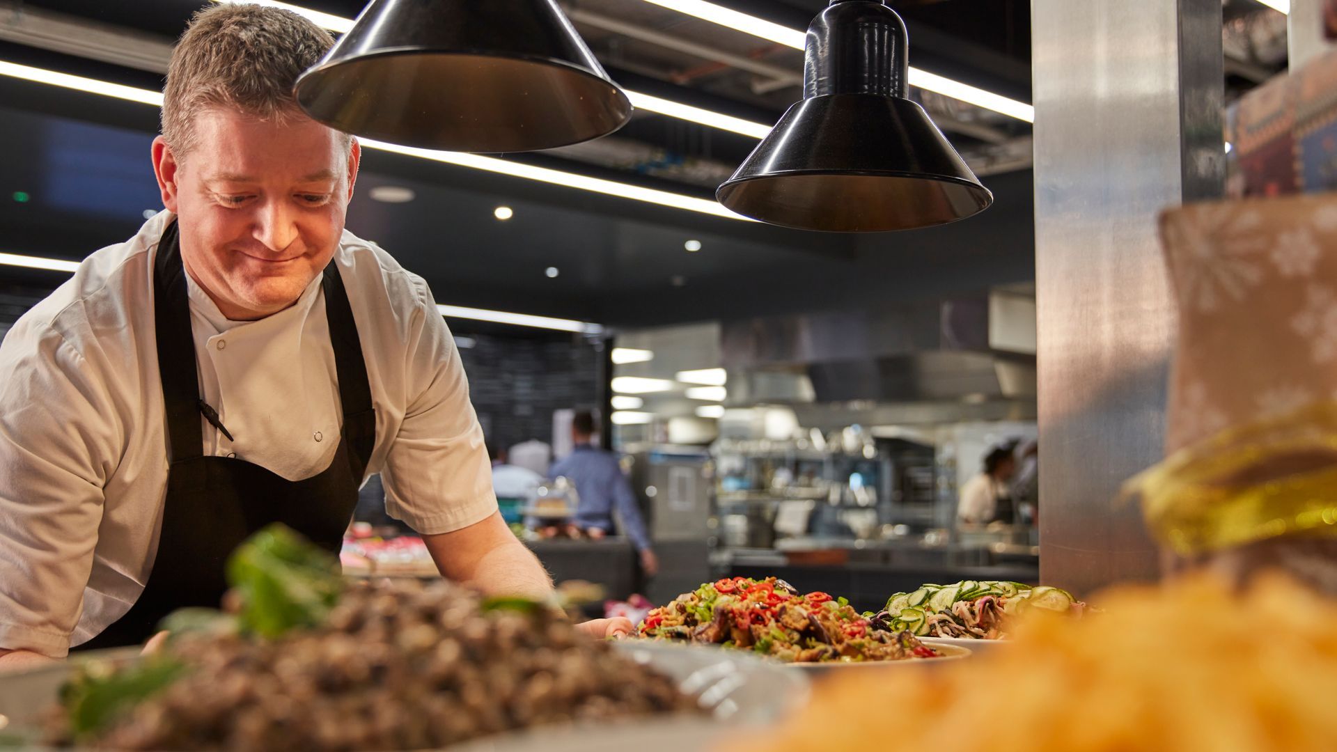 Chef preparing food at a bustling restaurant buffet under warm hanging lights