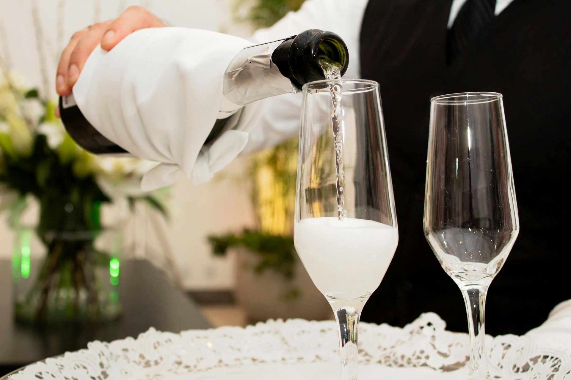 Champagne being poured into a flute beside an empty glass on a white tablecloth