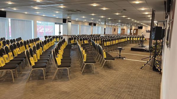 Empty conference hall with rows of yellow chairs and stage lighting under a low ceiling