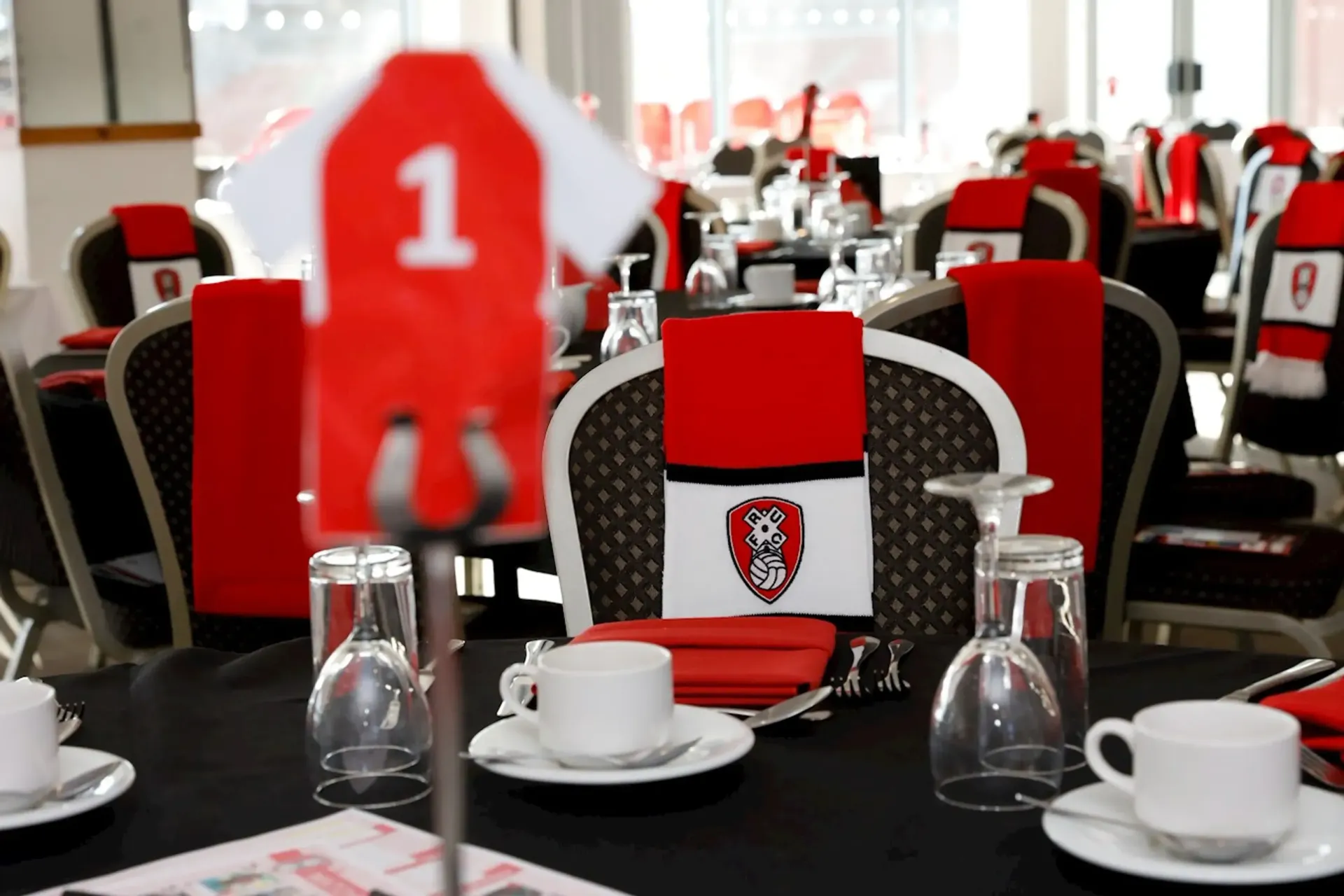 Red-and-black banquet table setting with numbered centerpiece and white cups, in a decorated event hall