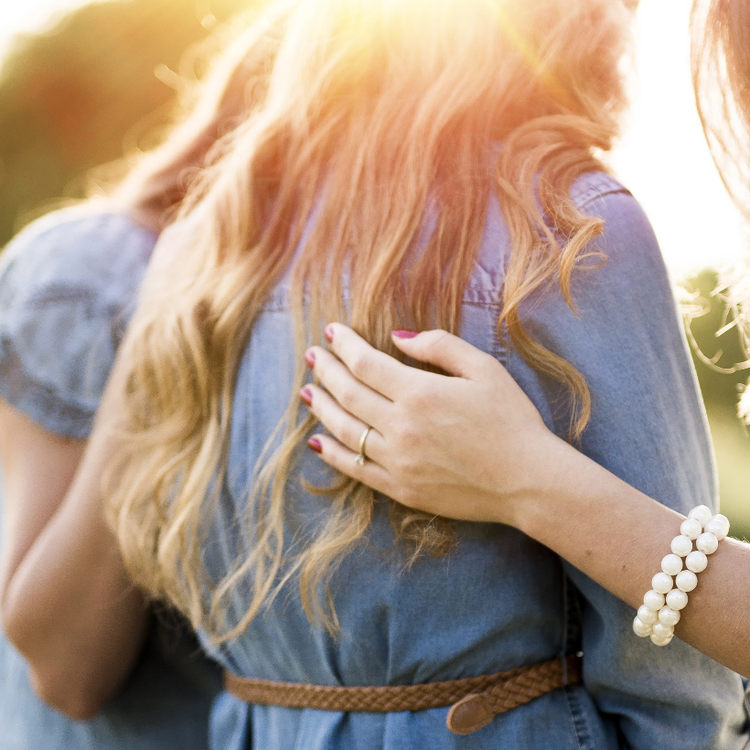 A woman wearing a pearl bracelet is hugging another woman