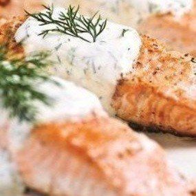 Seared salmon fillets topped with creamy dill sauce and fresh dill sprigs.