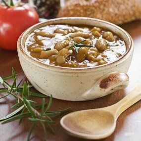Bowl of beans with rosemary, tomato, bread, and wooden spoon.