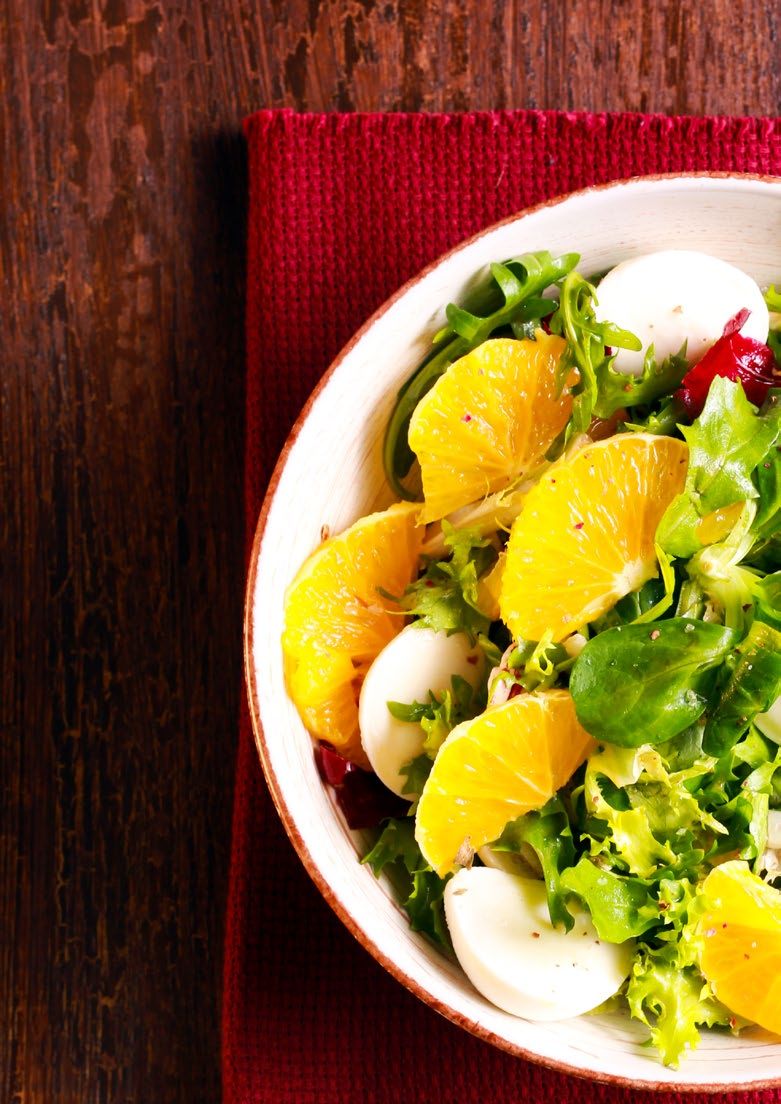 Salad with orange slices, mozzarella balls, and greens in a white bowl on a red placemat.
