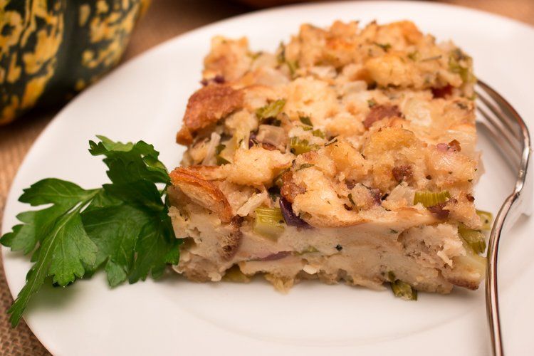 Slice of stuffing on a white plate with parsley and a fork; squash in the background.