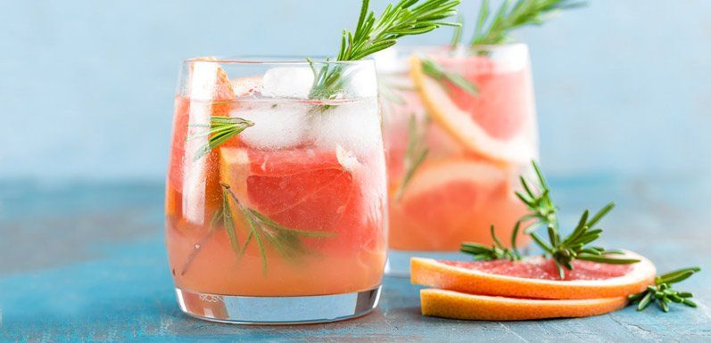 Two glasses of grapefruit cocktails with rosemary sprigs and grapefruit slices on blue background.