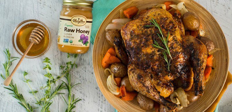 Roasted chicken with vegetables on a plate, honey jar, and honey dipper.