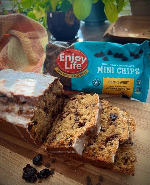 Chocolate chip bread slices, glazed, on a wooden board with an “Enjoy Life” chocolate chips bag.