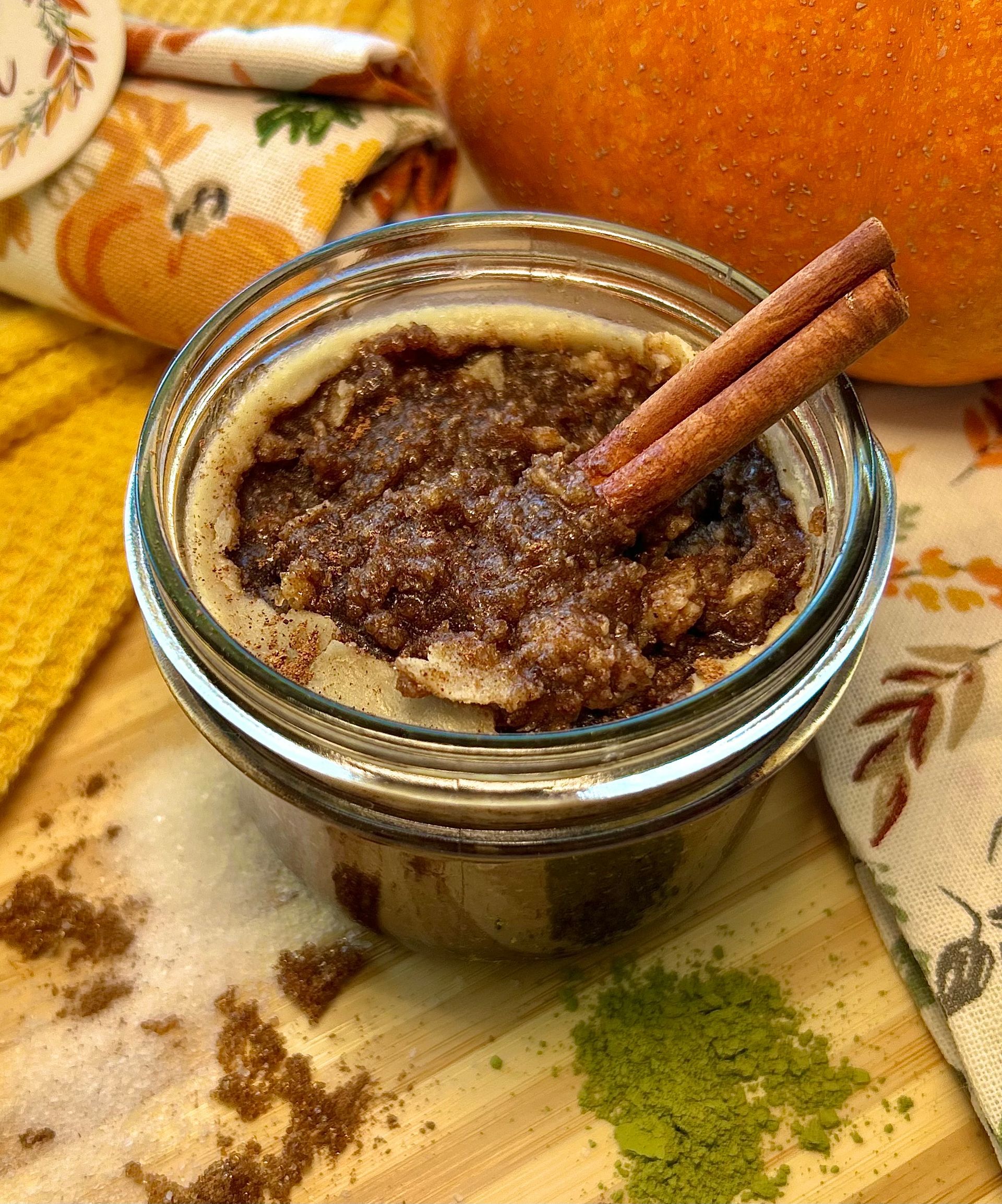Pumpkin dessert in a glass jar, topped with cinnamon sticks. Pumpkin and autumn-themed decor in the background.