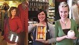 Three smiling people holding various items in a store; one has a helmet, another a gift, and the last a decorative ball.