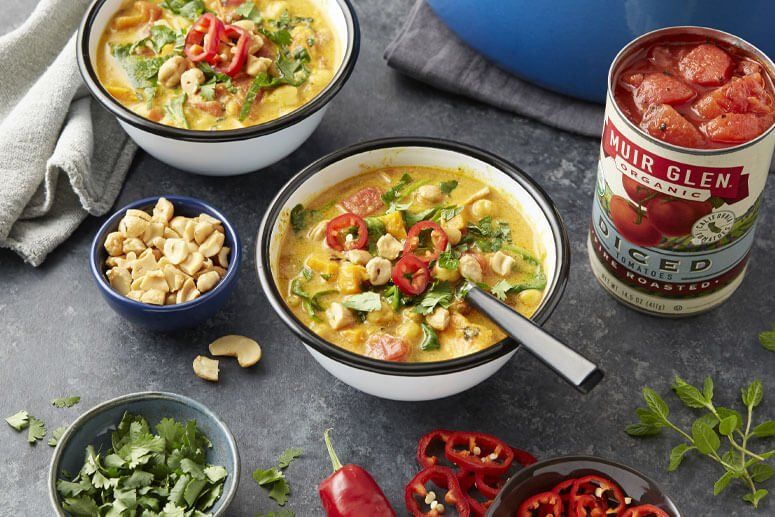 Bowls of yellow curry with toppings, ingredients including tomatoes and nuts.
