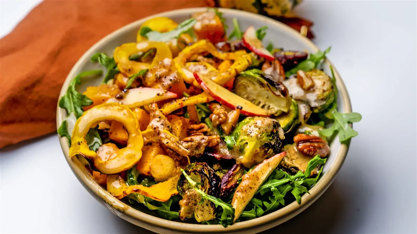Bowl of colorful autumn salad with roasted vegetables, arugula, and pecans.