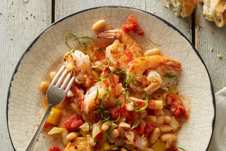 Shrimp and white bean dish on a textured plate with a fork; tomatoes and herbs visible.