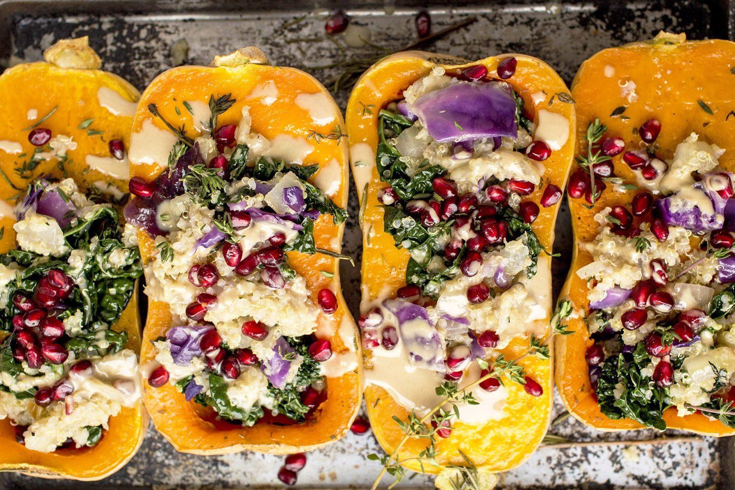Roasted butternut squash halves stuffed with kale, red onion, pomegranate seeds, and sauce on a baking sheet.