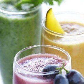 Three colorful smoothies in glasses, grapes in the foreground.