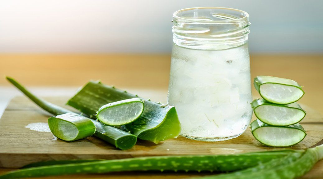 Aloe vera plant with lime slices on a wooden board next to a glass jar filled with liquid.