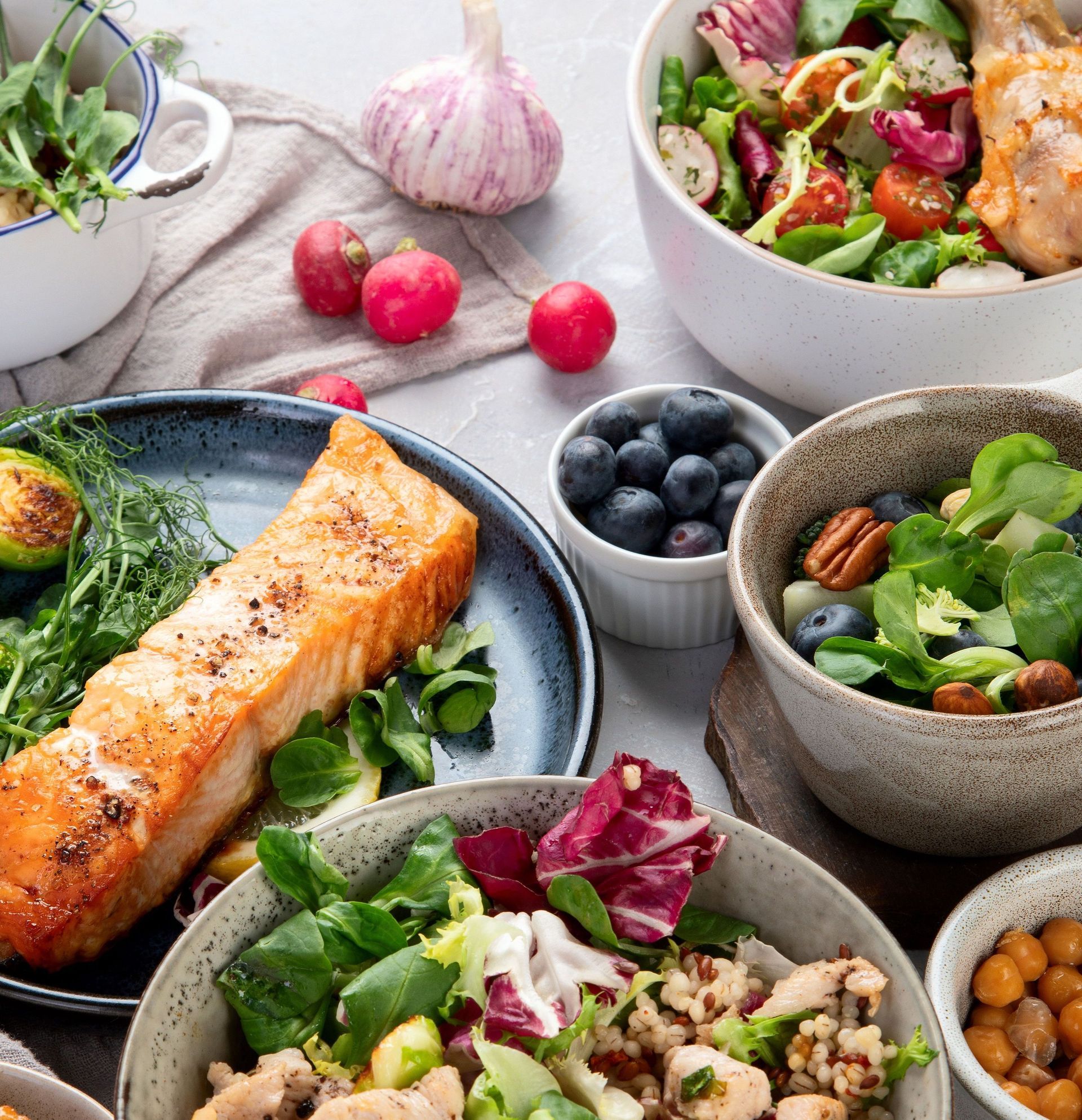Assortment of healthy food: grilled salmon, salads with vegetables, blueberries, nuts, and chickpeas. Fresh and colorful arrangement on a table.