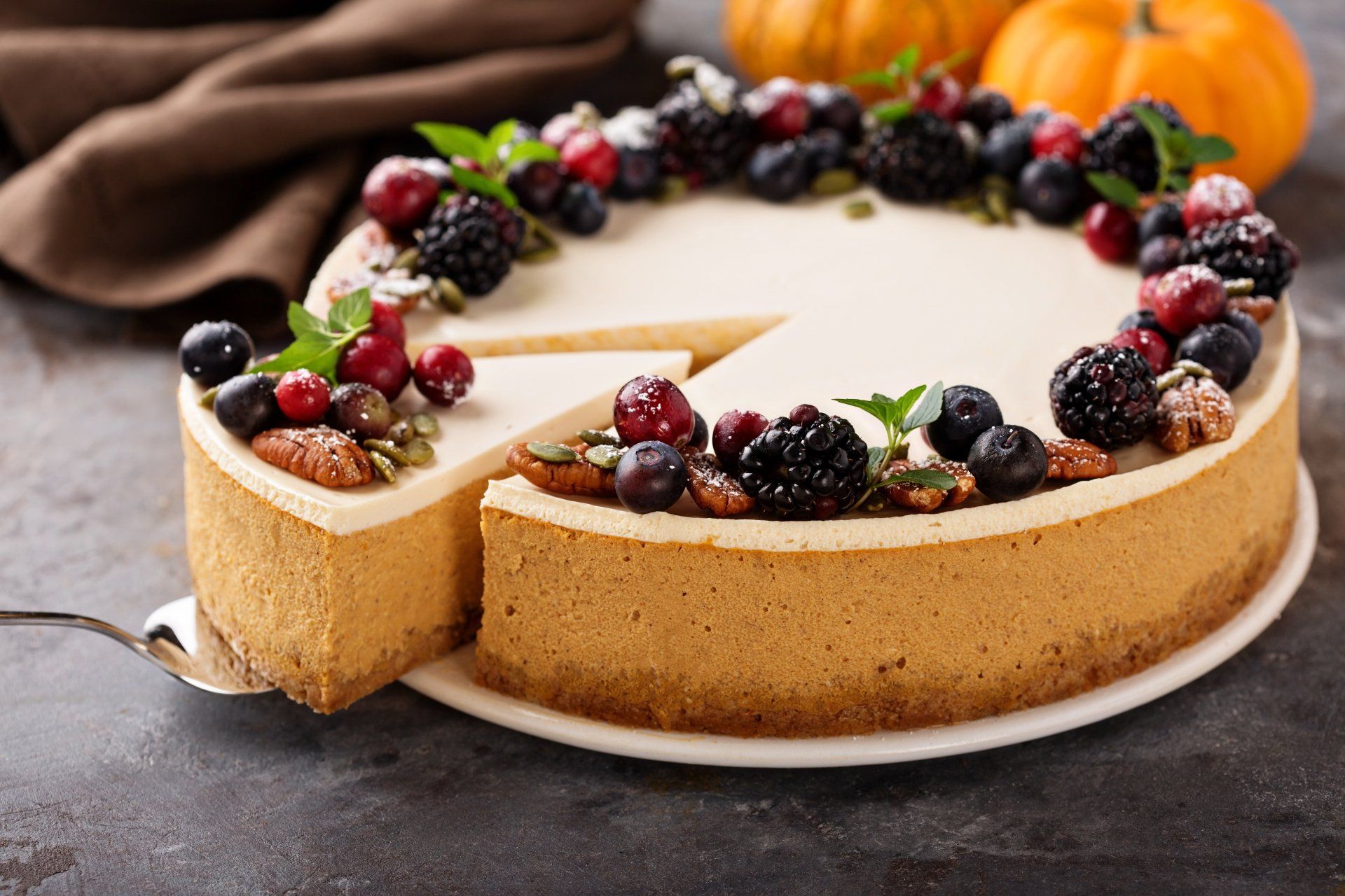 Pumpkin cheesecake with berries and nuts; slice being removed.