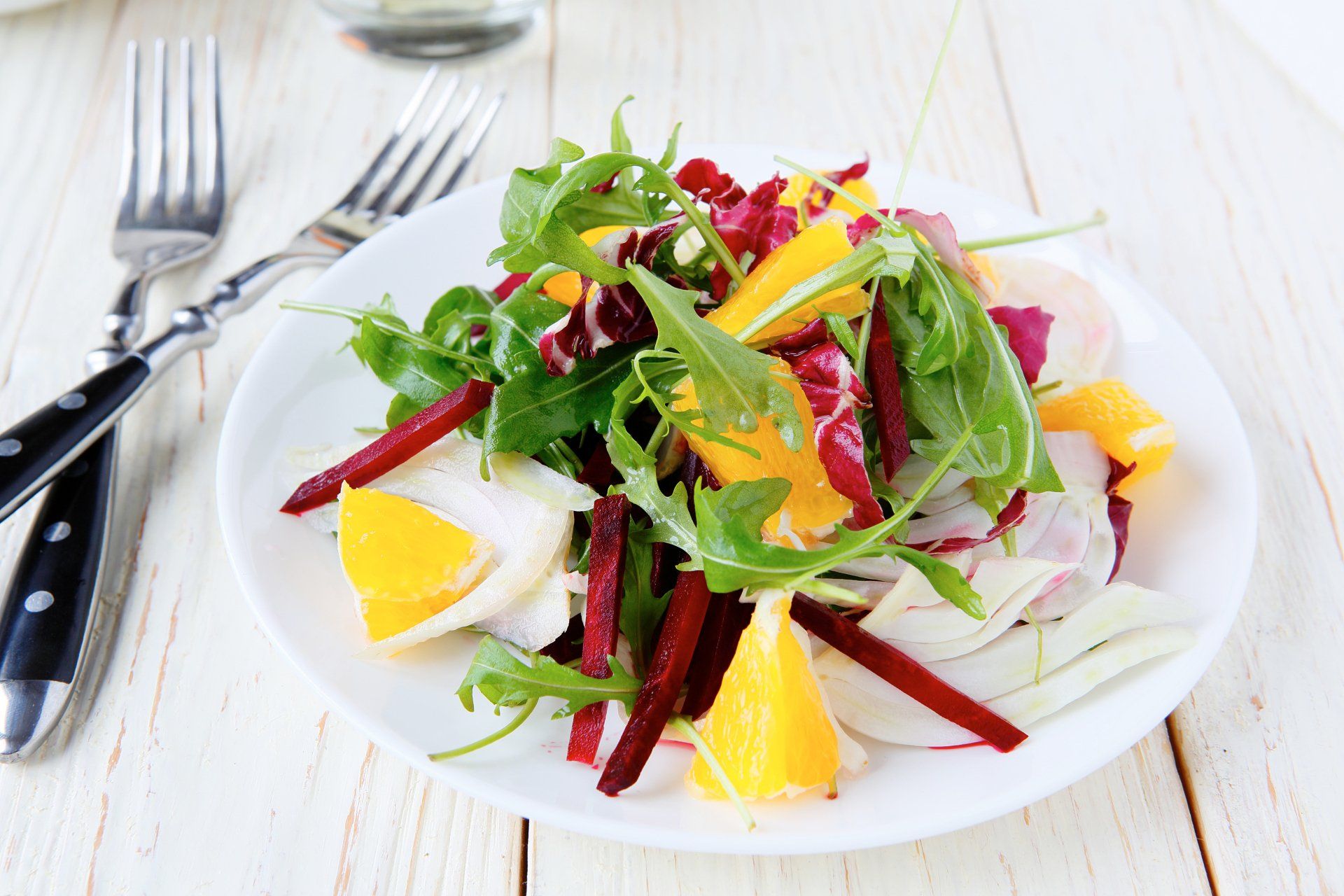 Salad with arugula, orange slices, red beets, and fennel on a white plate; forks beside.