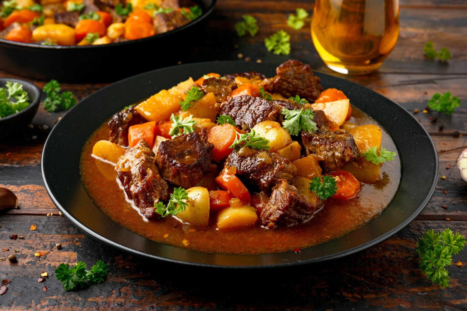 Beef stew with carrots and potatoes, served on a black plate with parsley garnish.