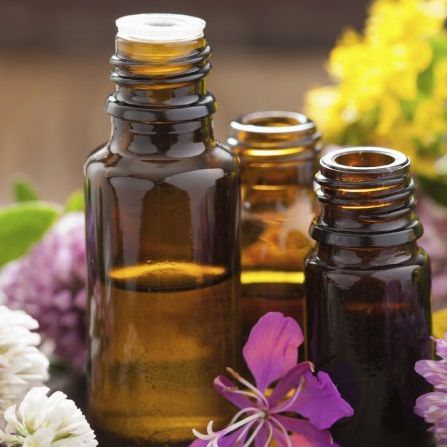 Three amber glass bottles of essential oil surrounded by colorful flowers.