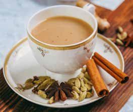 Cup of chai tea with spices on a saucer: cinnamon sticks, cardamom, star anise, on a wooden surface.