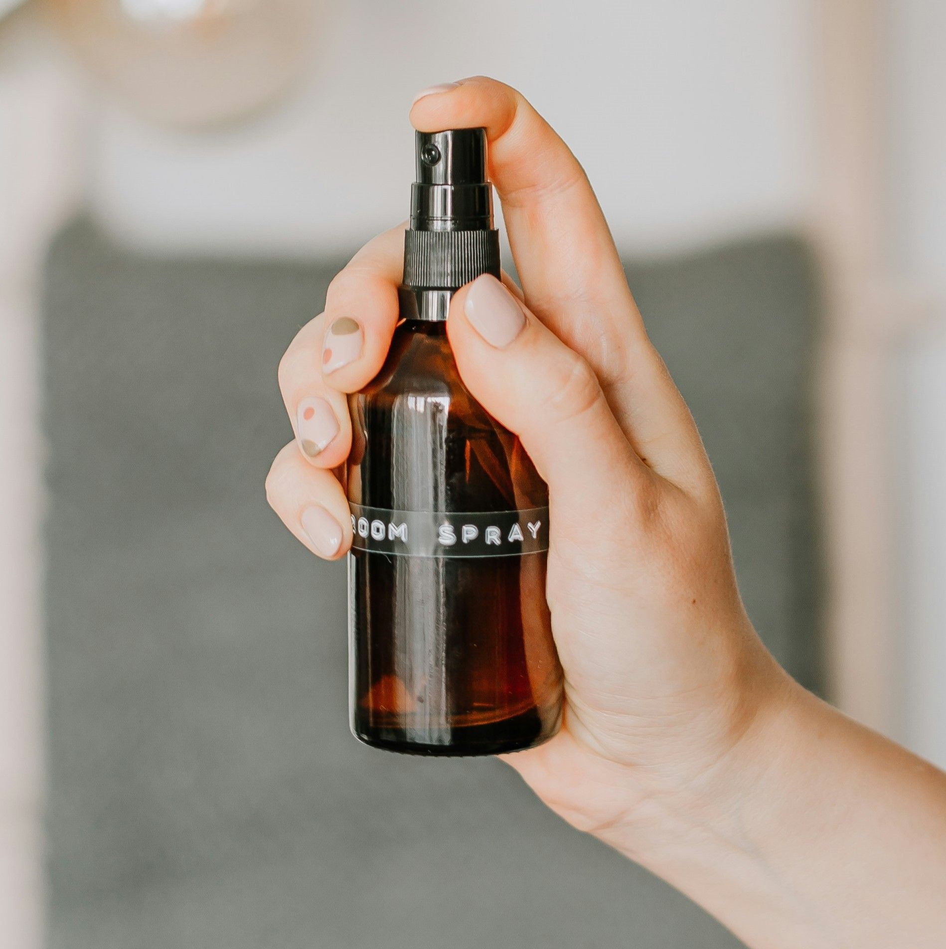 A hand holding a brown spray bottle labeled