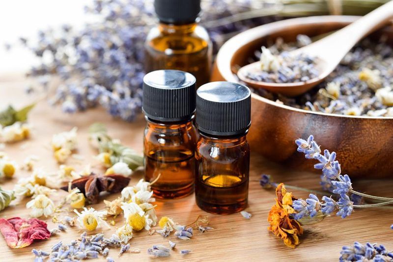 Bottles of essential oils surrounded by dried flowers and herbs, including lavender and chamomile.