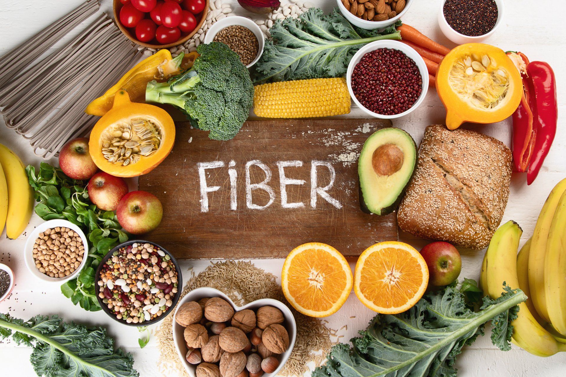 Variety of high-fiber foods, including fruits, vegetables, and grains, arranged around a wooden board that says