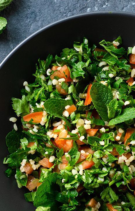 Tabbouleh salad in a black bowl: bright green parsley, mint, diced tomatoes, and bulgur wheat.