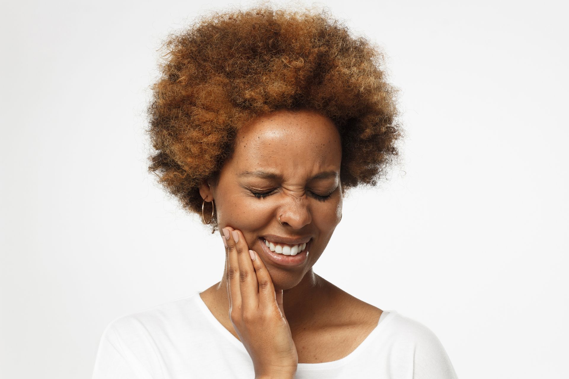 A Black woman with an afro holds her jaw, showing a painful expression against a white background.