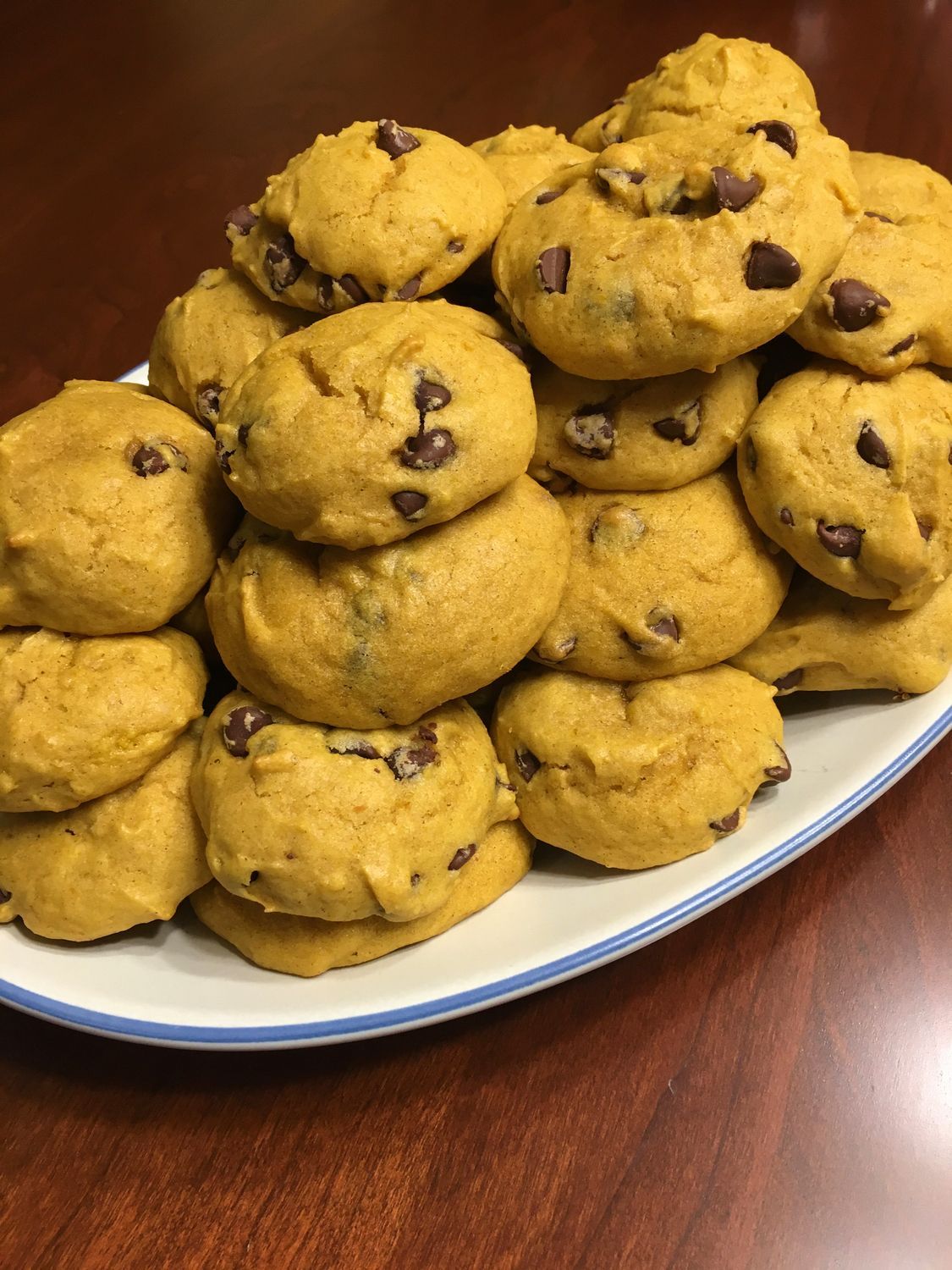 Pile of pumpkin cookies with chocolate chips on a white plate with blue trim.