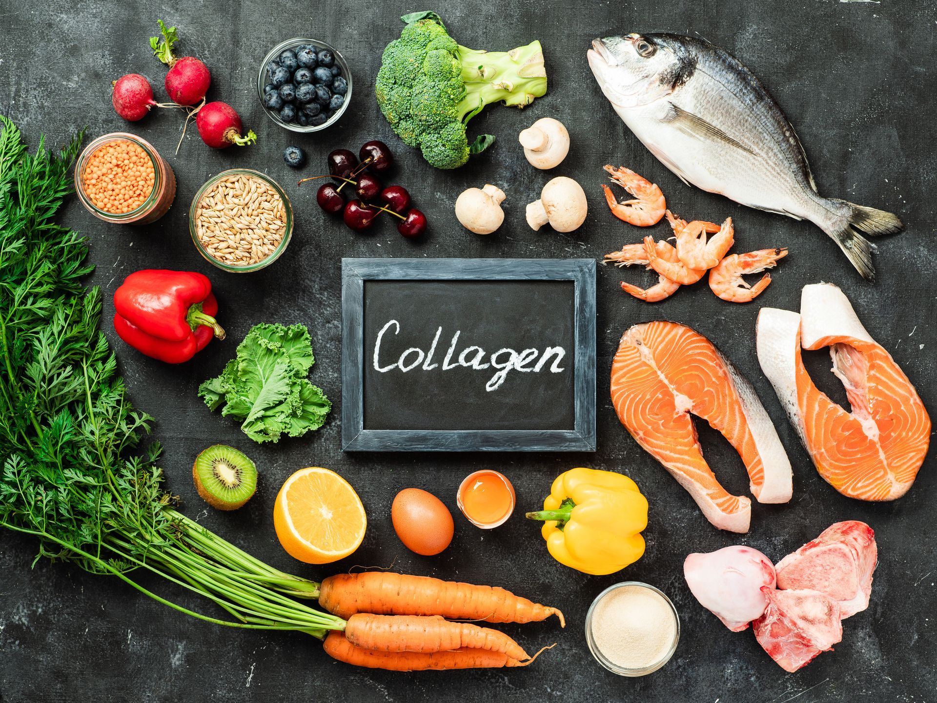Assortment of foods, including fish, vegetables, and fruit, arranged around a chalkboard that reads