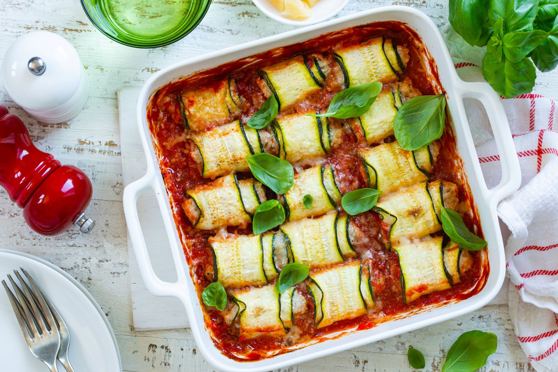 Zucchini rollatini baked in a white dish with tomato sauce and basil leaves.