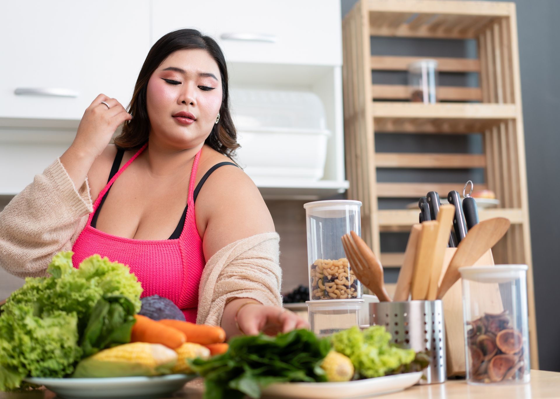 Woman in a pink apron in a kitchen preparing vegetables, reaching for a leaf of lettuce.