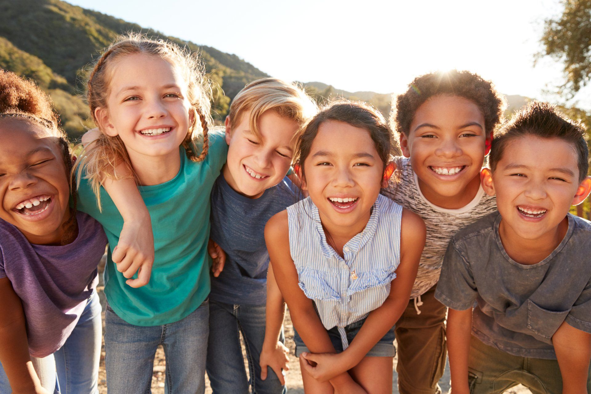 Six diverse children smiling and embracing outdoors.
