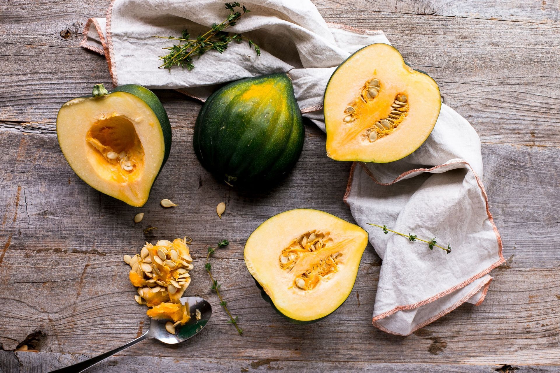 Acorn squash halves, whole squash, seeds, and thyme on a wooden table.