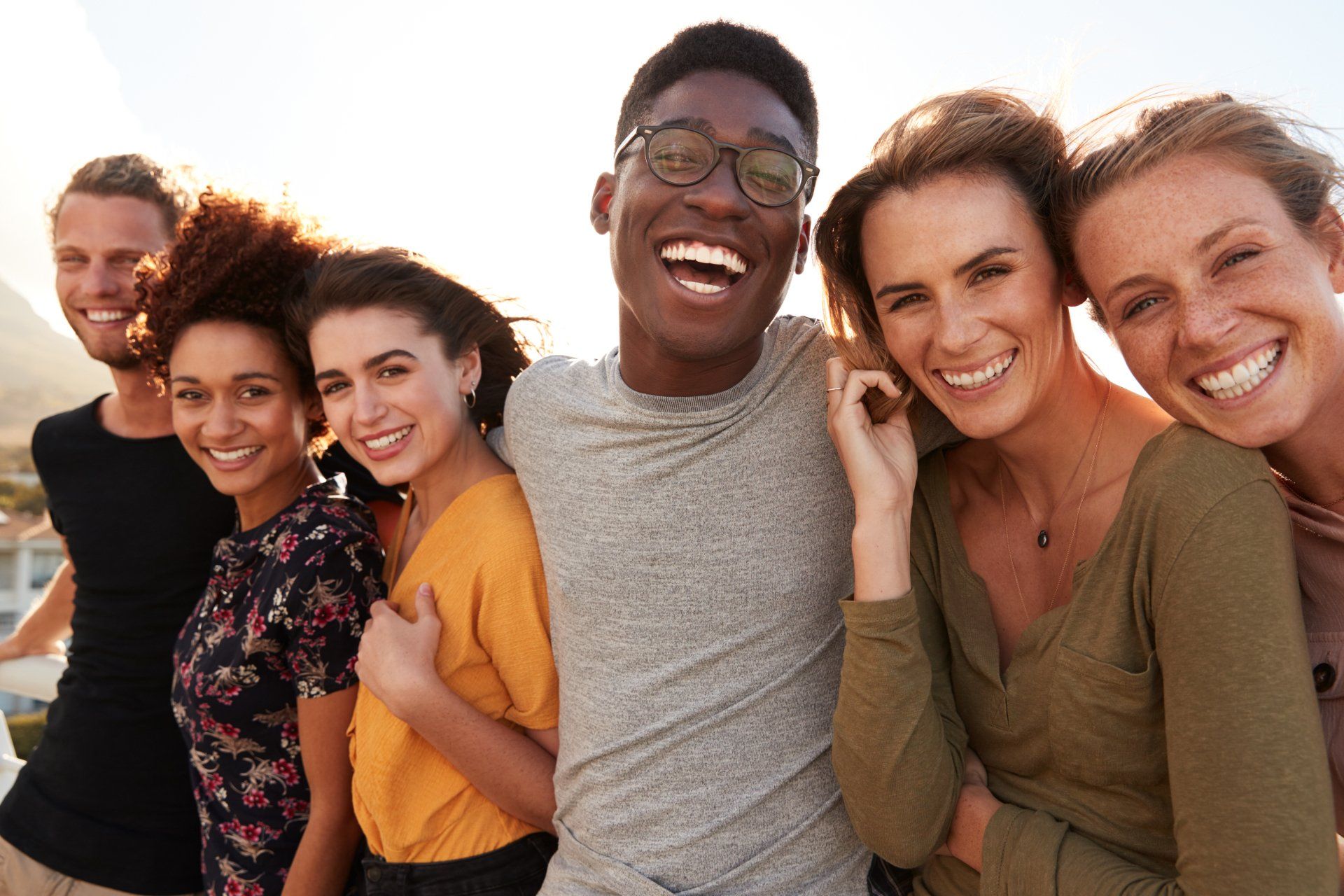Group of six diverse friends smiling and laughing outdoors.