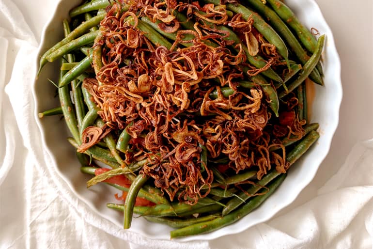 Green beans topped with crispy fried onions in a white bowl.