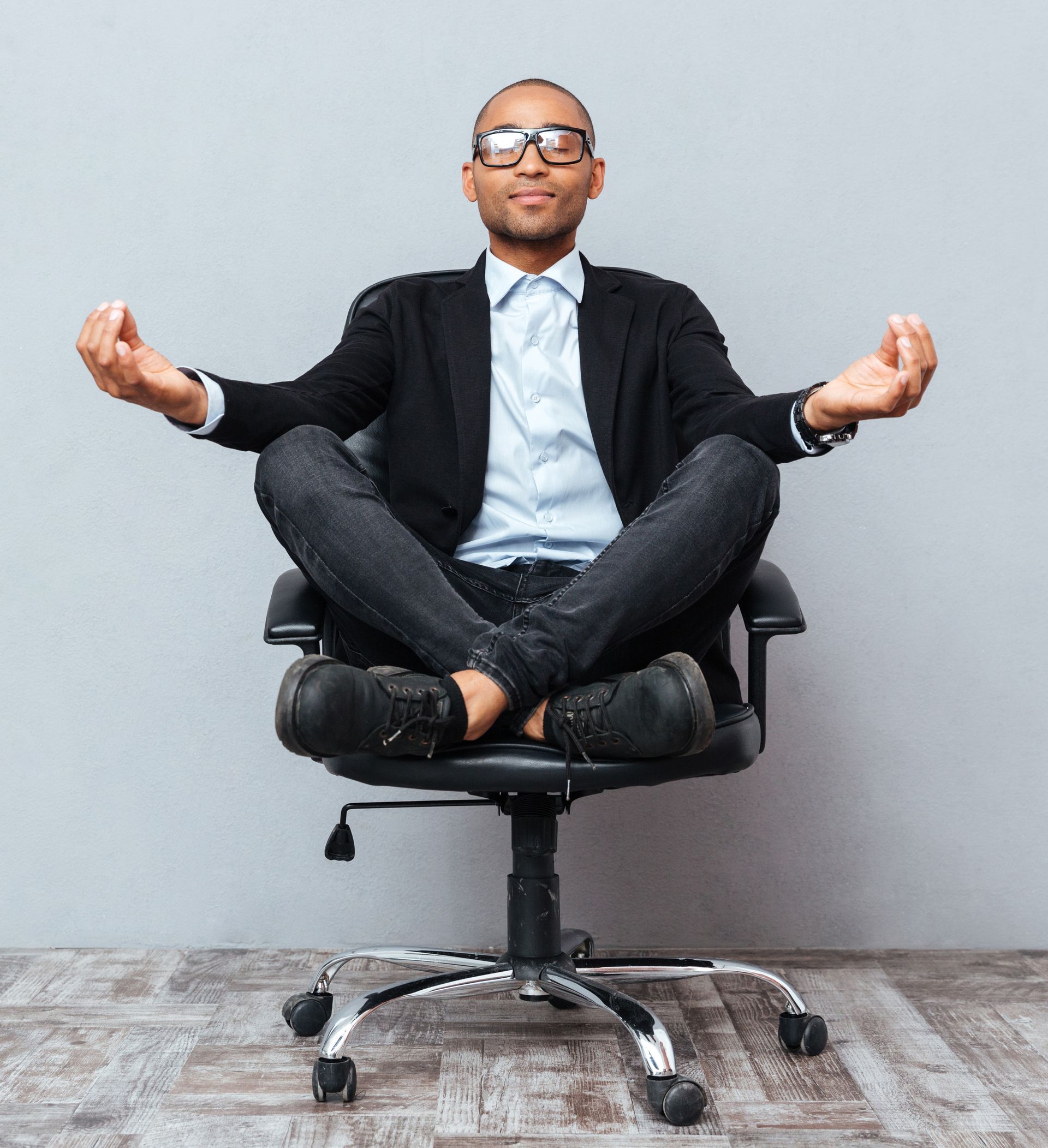 Man in suit meditating in office chair, hands in mudra, eyes closed.
