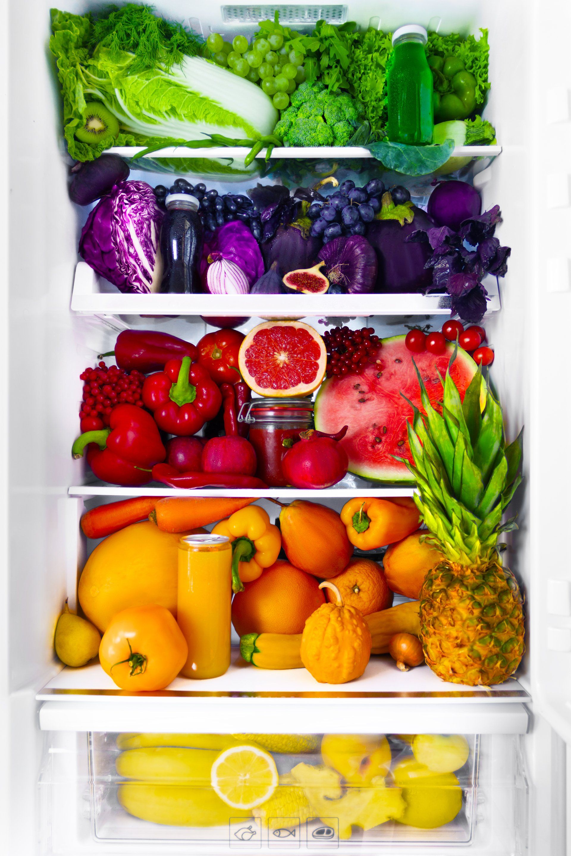 A refrigerator filled with fruits and vegetables arranged in a rainbow of colors. From top to bottom: green, purple, red, orange, and yellow.