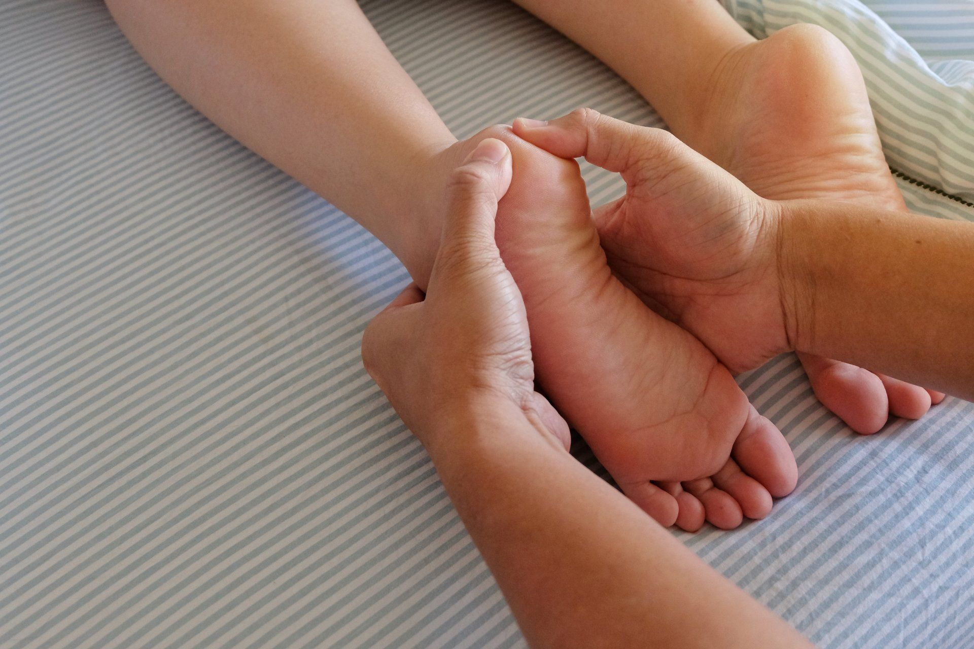 Hands massaging a foot, lying on a striped surface. Close-up of the foot's sole being worked on.