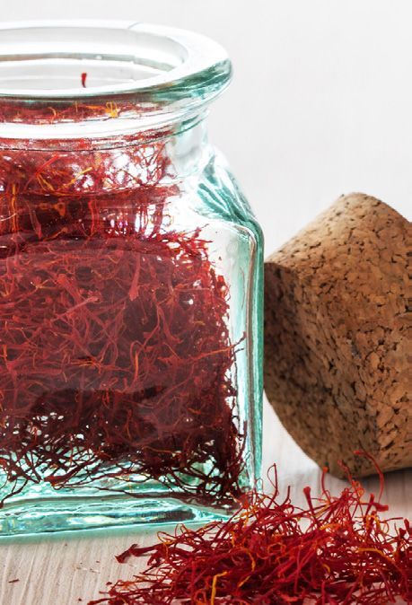 A glass jar filled with red saffron threads, next to a cork stopper and a small pile of saffron.