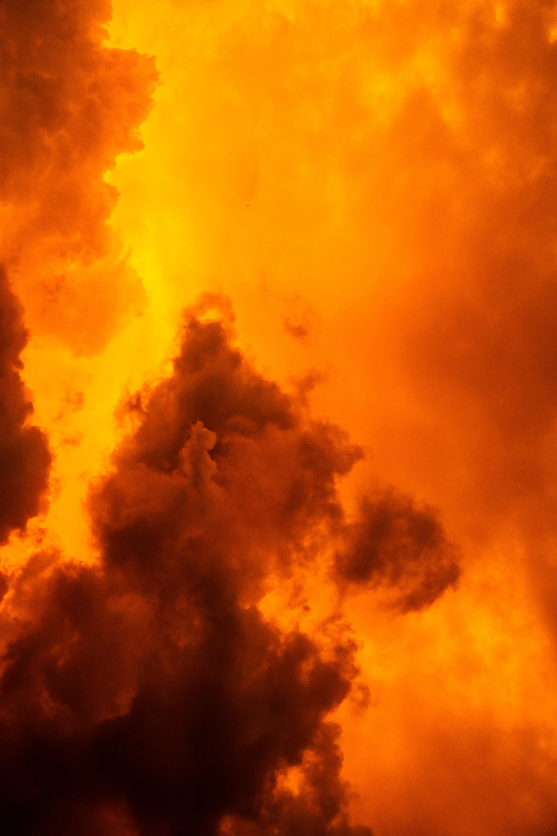 Fiery, orange sky with dark, billowing clouds; dramatic and ominous.