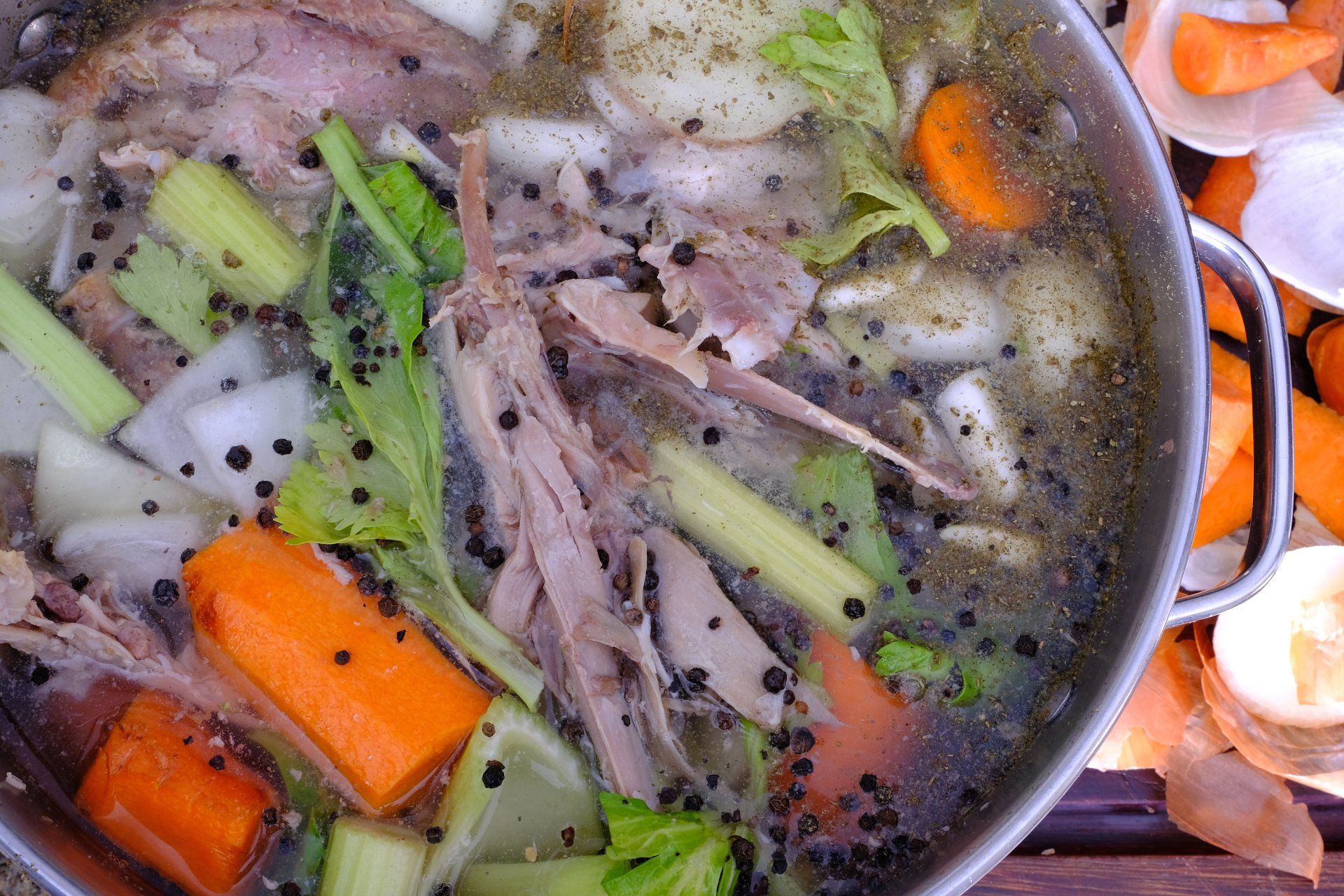 Chicken stock simmering in a pot with vegetables, black peppercorns, and meat.