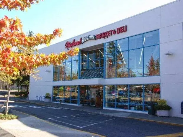 A large grocery store exterior with blue windows under a bright sky; a fall tree in the foreground.