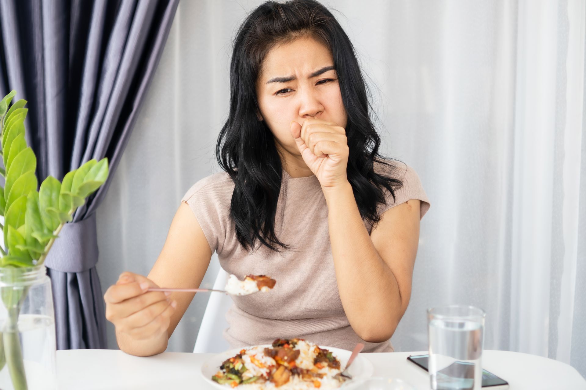 Woman coughing while eating food at a table; appears unwell.