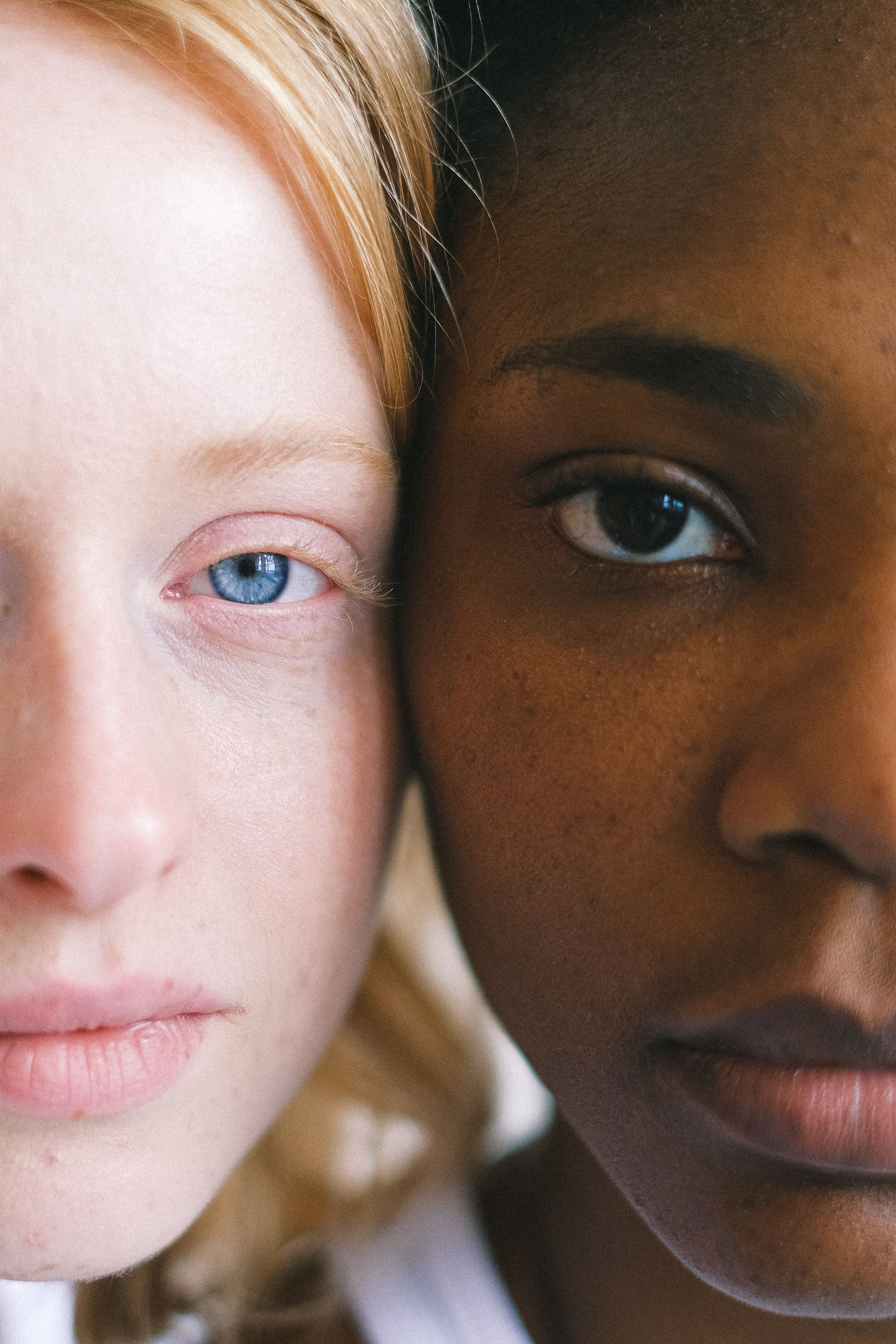 Two women, one with pale skin, blue eyes, and blonde hair, the other with dark skin and dark eyes, face together.