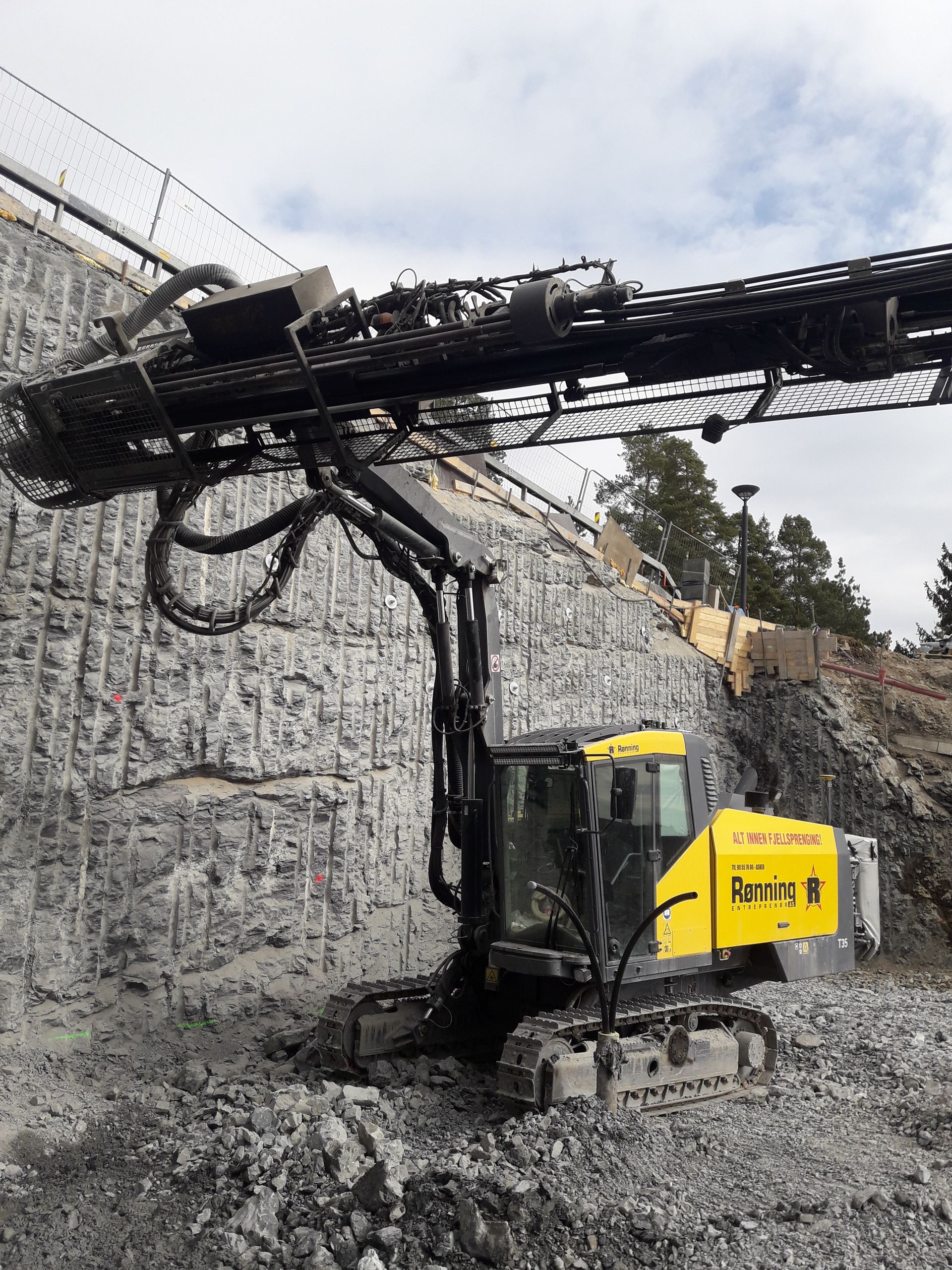 Gul og svart fjellboremaskin på en steinete skråning, borer inn i en vegg.